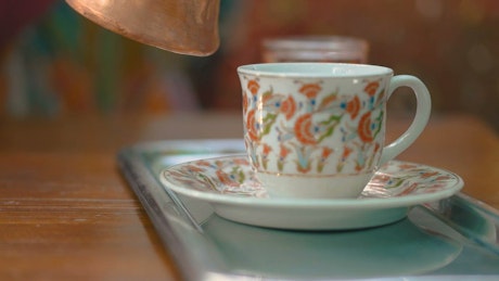 Turkish coffee being poured into a decorated cup.
