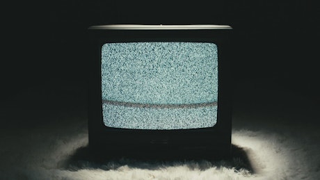 TV static playing on a TV screen in a dark room.