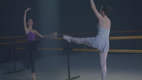 Two ballet dancers practicing at the bars.