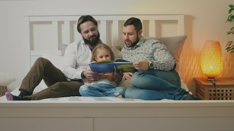 Two fathers reading their child a bedtime story at night.