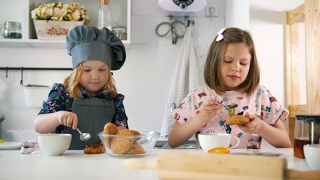 Two girls in the kitchen eating cookies with jam