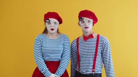 Two mimes having a laugh in costume on a yellow background.