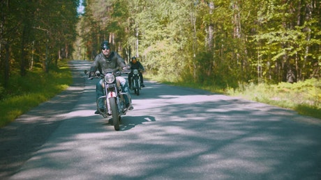 Two motorcyclists riding on a road in a forest.