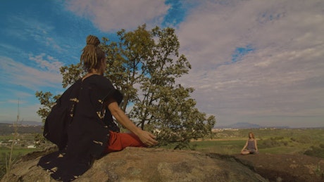 Two people meditating on huge rocks outdoors.