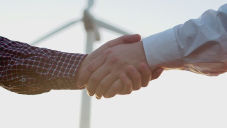 Two people shaking hands in front of a wind turbine.