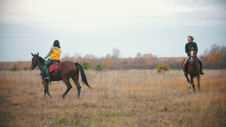 Two women circling on horseback in a large field.