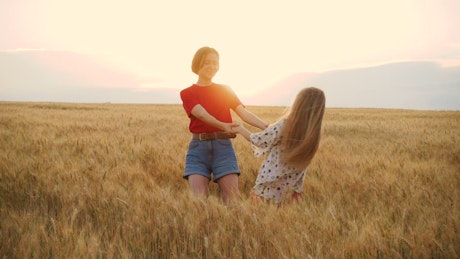 Two young girls spinning in a wheatfield.