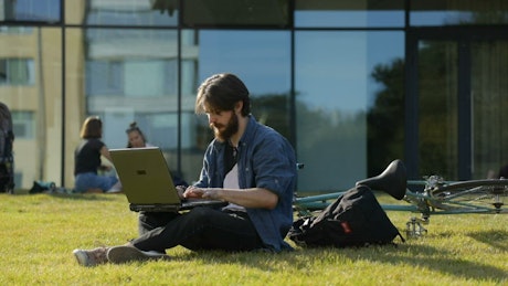 University student sitting outside with laptop on grass