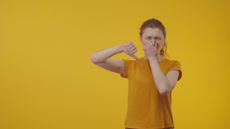 Upset woman shows thumbs down gesture against a yellow background.