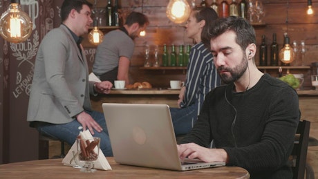 Urban man typing on laptop is served coffee in hip cafe