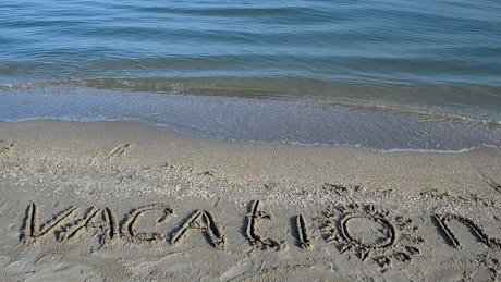 "Vacation" written on the beach near the sea water