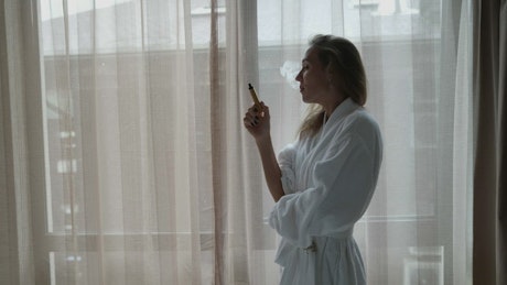Vaping in a hotel room by a window in a robe.