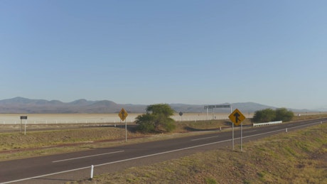 Various vehicles traverse the asphalt highway beside the breathtaking desert landscape in the background.