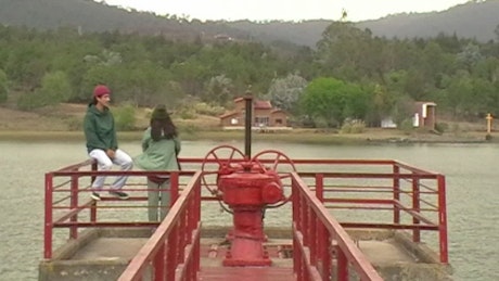 Vintage looking footage of a young couple laughing on a metal pier with the lake and mountains in the background..