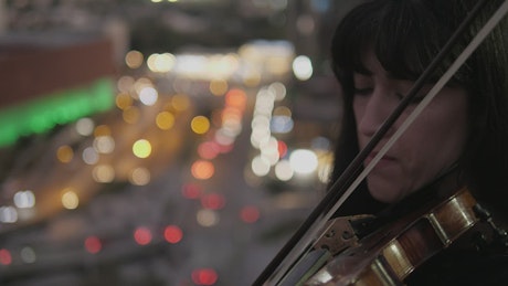 Violinist playing on city rooftop at dusk.