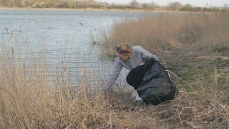 Volunteer picking up trash by the river