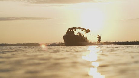 Wakeboarder riding behind boat at sunrise.