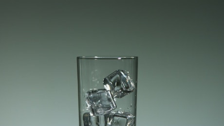 Water drops falling into a glass with ice cubes.