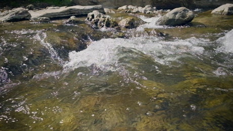 Water in slow motion flows down the river creating a foam and waves through the rocks.