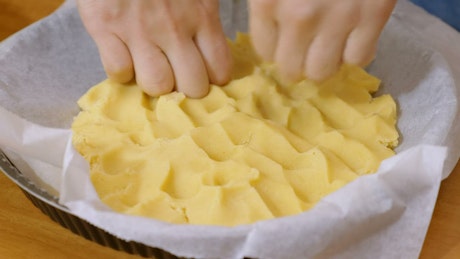 White hands pressing pastry base into a baking pan.