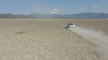 White van crossing a desert in an aerial shot.