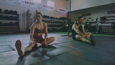 Woman and man stretching in a gym.