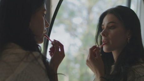 Woman applying makeup in front of a mirror.