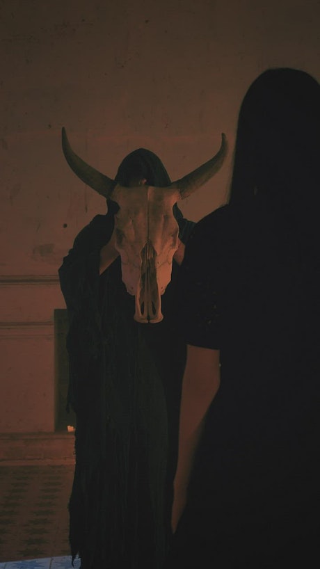 Woman bows to the skull of a bull holding a hooded man.
