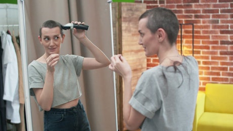 Woman cautiously shaving her head in front of a mirror.
