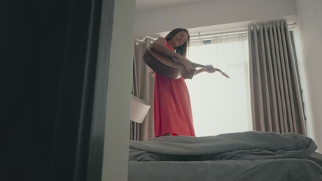 Woman dancing on the bed and playing the guitar.