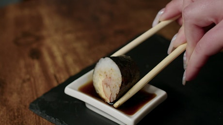 Woman dipping a piece of sushi in soy sauce.