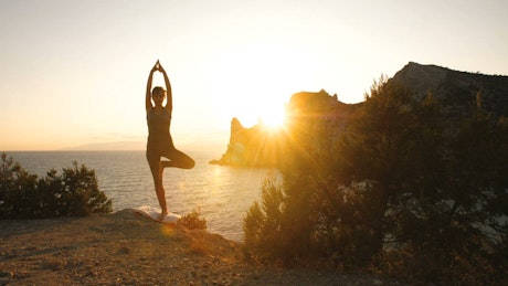 Woman doing yoga by the sea at sunset.
