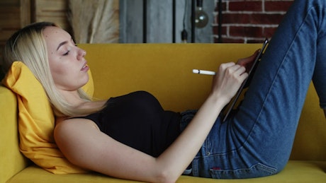 Woman drawing casually on a tablet on the couch.