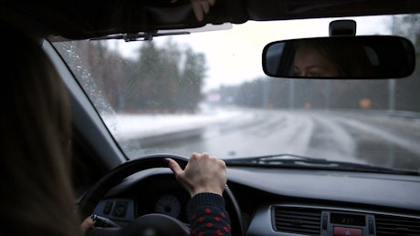 Woman driving down a lonely road on a snowy day.