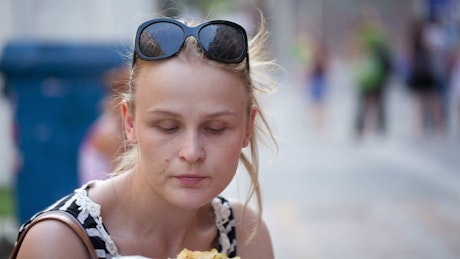 Woman eating fast food in the street.