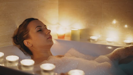 Woman enjoying a relaxing bubble bath surrounded by candles.