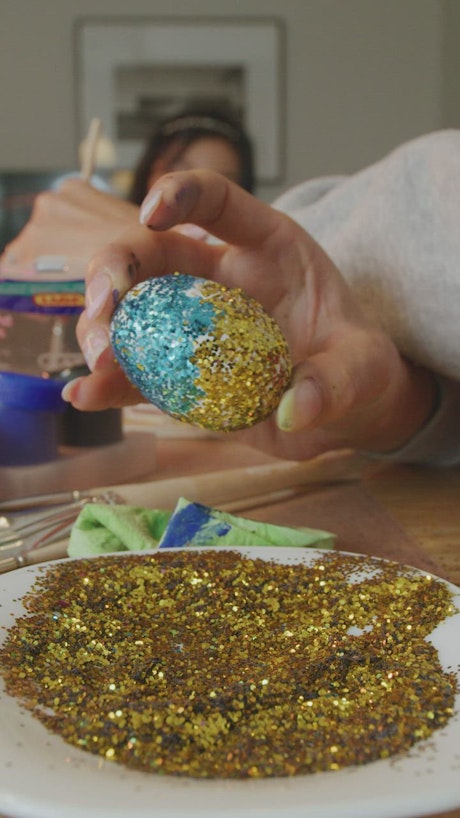 Woman gluing glitter to an easter egg.