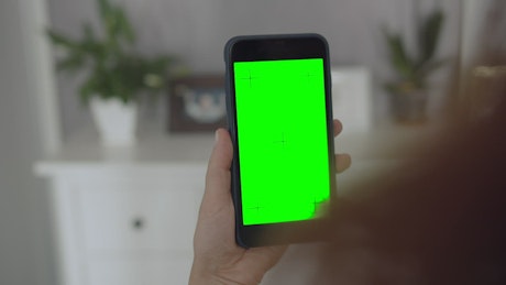Woman holding greenscreen mobile phone taps screen.