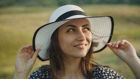 Woman holding her hat in a meadow.