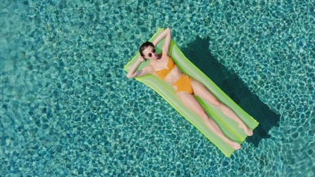 Woman in an orange bikini sunbathing on a pool toy.