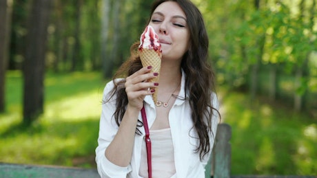 Woman licking an ice cream cone in the park.
