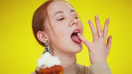Woman licking frosting off of her fingers from a cupcake.