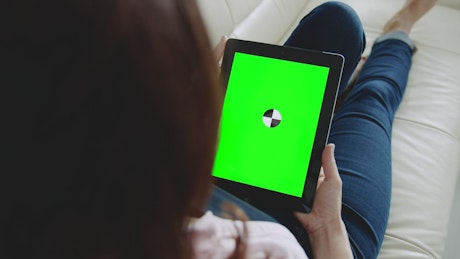 Woman looks at website with chroma key tablet on sofa.
