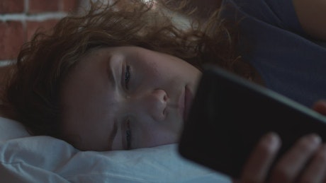 Woman lying in bed looking at her phone in the dark.