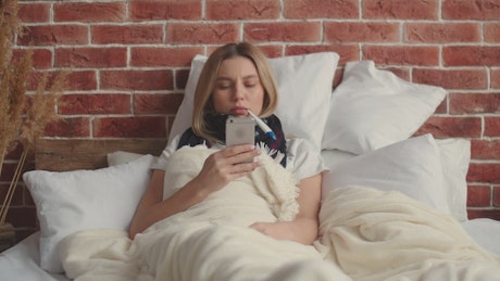 Woman lying in bed on her phone sick.