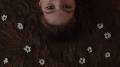 Woman lying on the ground surrounded by her hair filled with daisies.