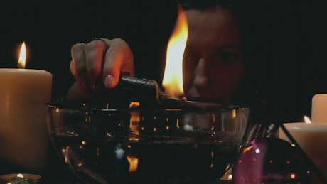 Woman moving a lit candle over a bowl in a spiritual ritual.