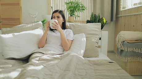 Woman opens video call on futuristic hologram panel in bed.