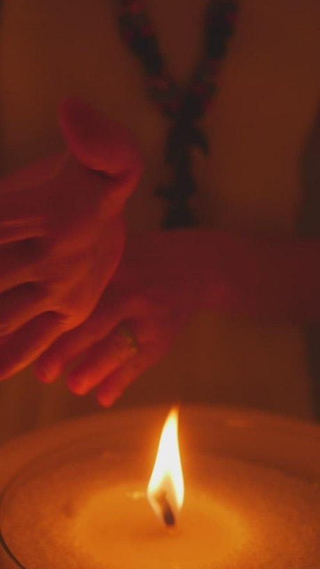 Woman passing her hands near the flame of a candle.