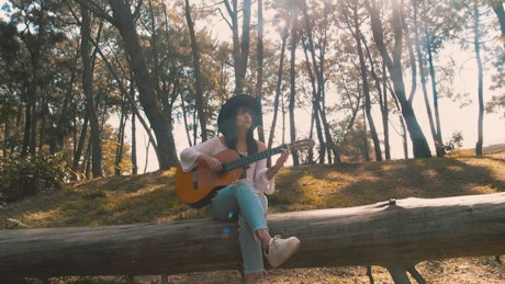 Woman playing guitar on a fallen log.